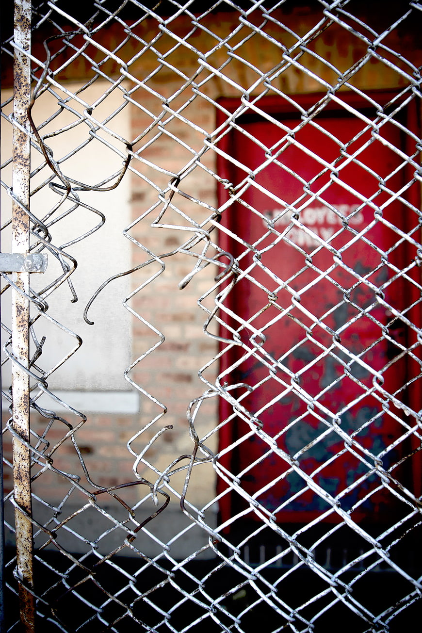Damaged Chain Link Fence with Red Door Background
