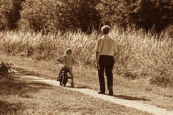 Senior man walking behind child riding bicycle on rural dirt path