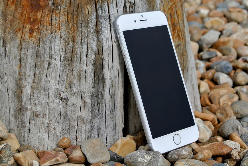 White Smartphone Leaning Against Weathered Wood on Pebble Beach