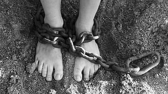 Black and white photo of shackled feet in sand