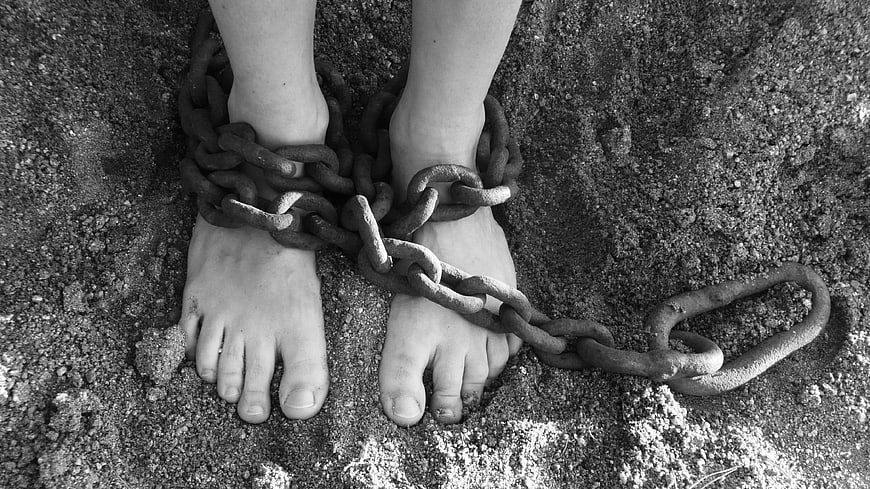 Black and white photo of shackled feet in sand