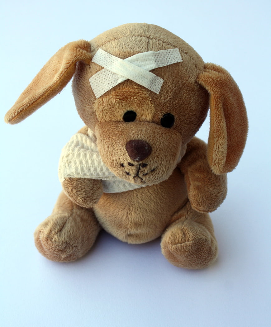 Injured Brown Plush Dog Toy With Bandages On Light Blue Background