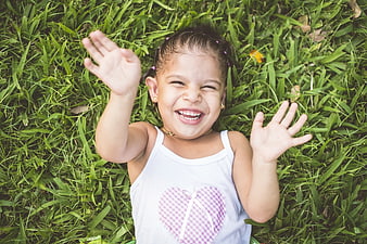 Happy little girl lying in grass waving hands