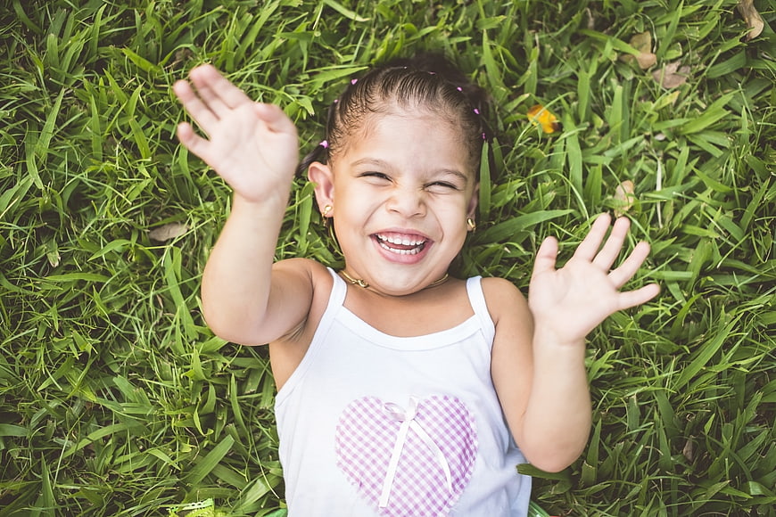 Happy little girl lying in grass waving hands