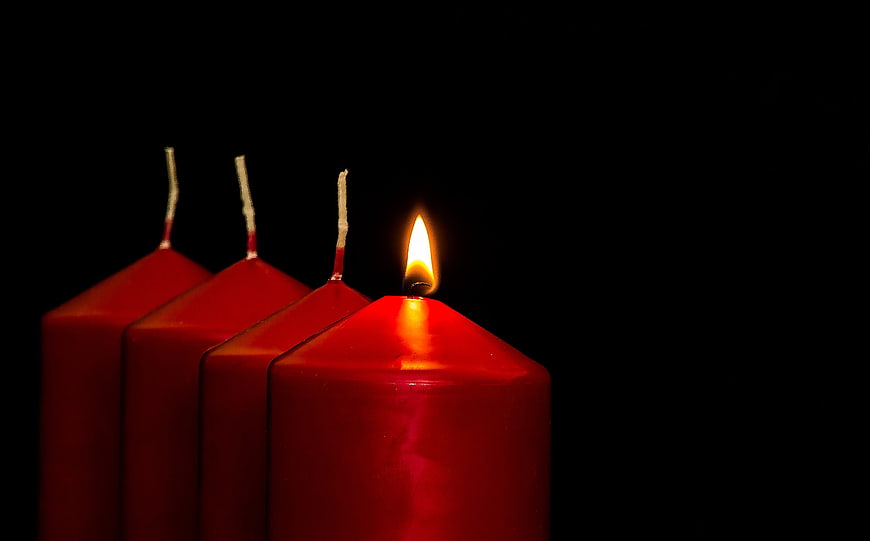 Four red candles with one lit flame on black background