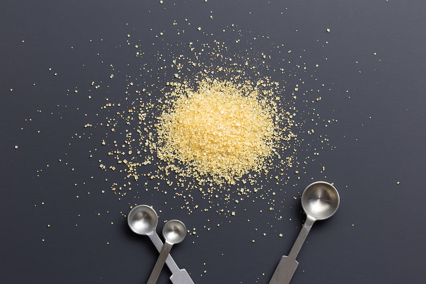 Top view of brown sugar pile with measuring spoons on dark background