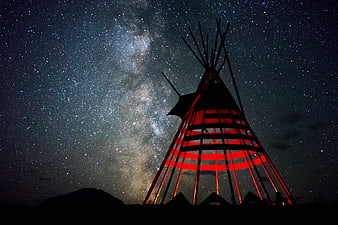 Red illuminated tipi silhouette against Milky Way night sky