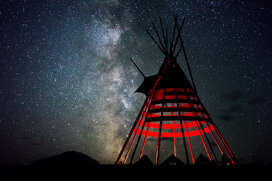 Red illuminated tipi silhouette against Milky Way night sky