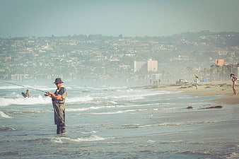 Man Fishing in Ocean Waves with Coastal City Background