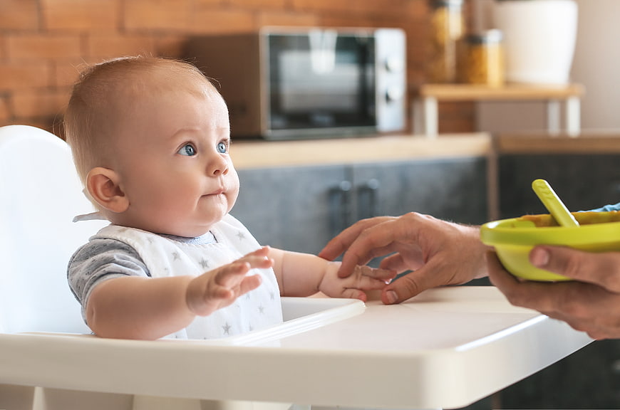 Baby in High Chair Reaching for Food Bowl