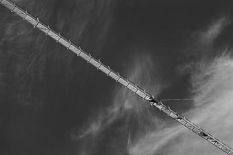 Black and white aerial view of suspension bridge through clouds