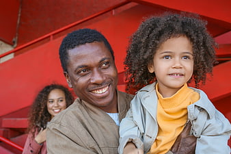 Happy Black Father Holding Daughter on Red Stairs