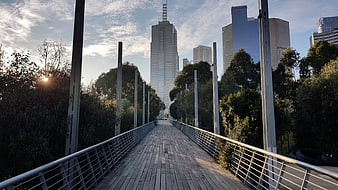 Wooden pedestrian bridge leading to city skyscrapers at sunset