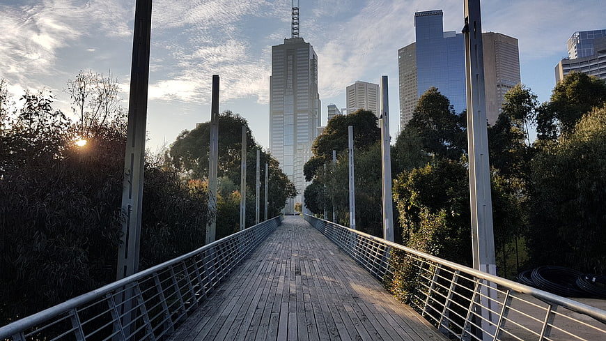 Wooden pedestrian bridge leading to city skyscrapers at sunset