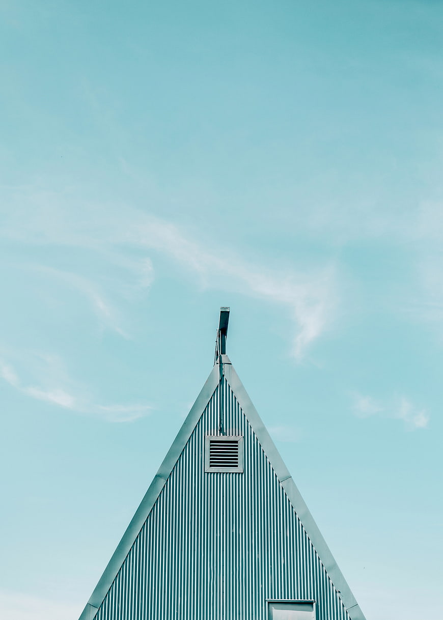 Teal corrugated metal roof peak against blue sky
