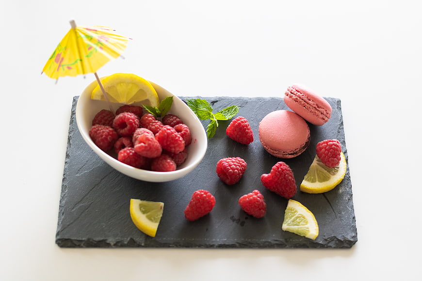 Fresh raspberries, lemon slices, and pink macarons on a slate board