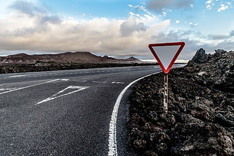 Yield sign on empty asphalt road in volcanic landscape