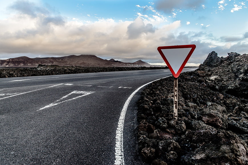 Yield sign on empty asphalt road in volcanic landscape
