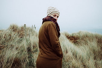 Woman in brown coat and beanie standing in coastal dunes
