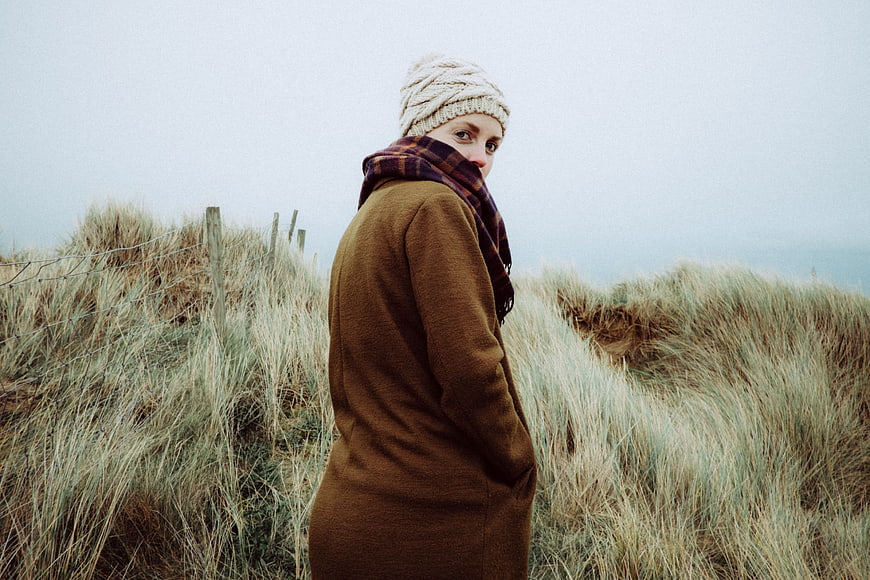 Woman in brown coat and beanie standing in coastal dunes