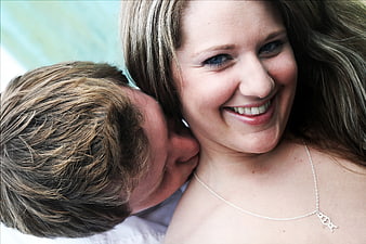 Happy couple kissing outdoors with woman smiling at camera