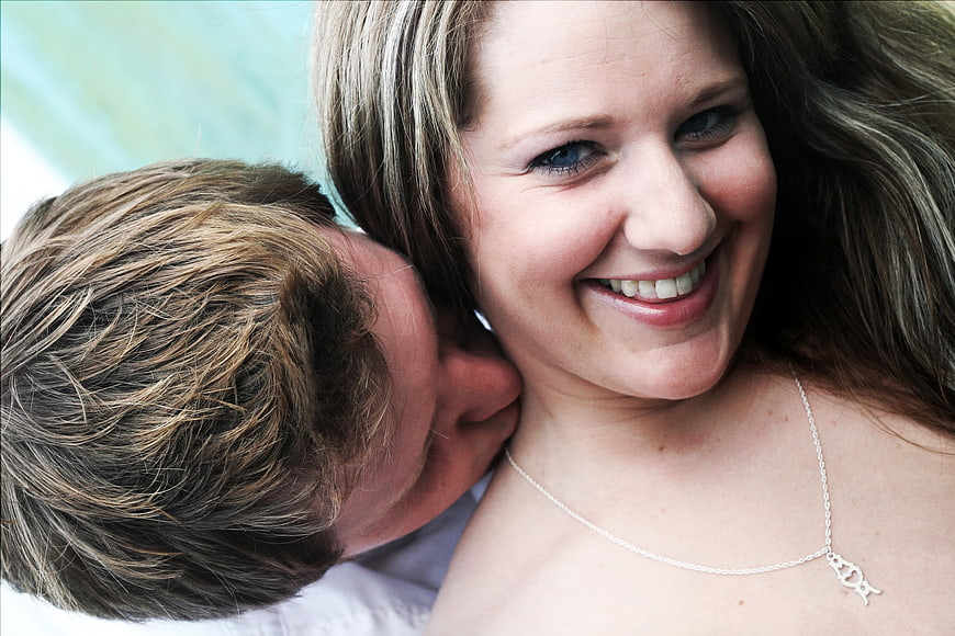 Happy couple kissing outdoors with woman smiling at camera