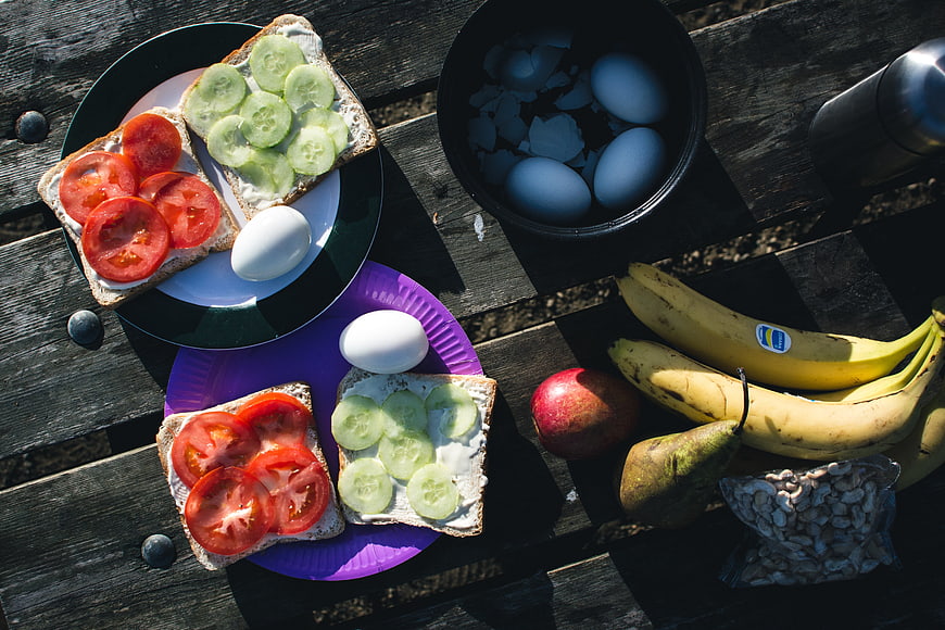 Healthy camping breakfast with sandwiches, eggs, and fruit on wooden table