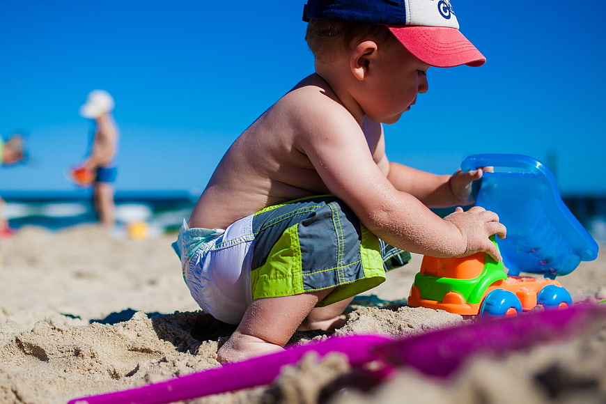 Toddler playing with colorful sand toys on sunny beach