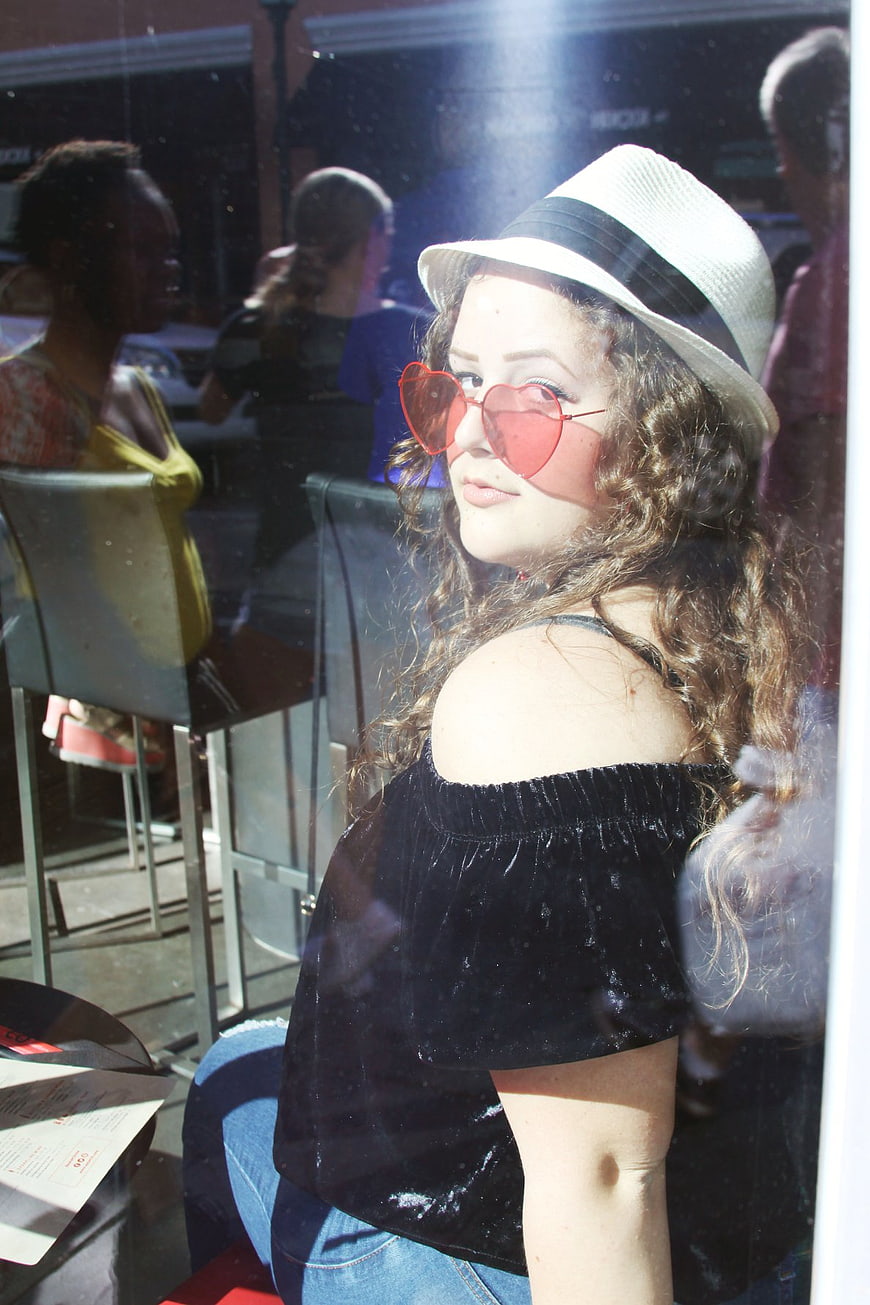 Woman with Heart Sunglasses and Fedora in Cafe
