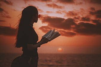 Silhouette of Woman Reading Book at Sunset by the Sea