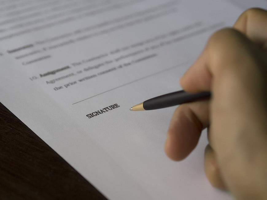 Hand holding pen ready to sign business contract document