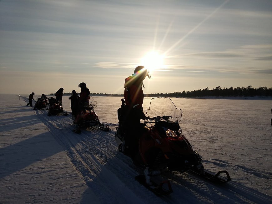 Snowmobile riders silhouetted against winter sunset on frozen lake