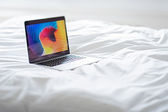 Laptop on white bed sheets for remote work