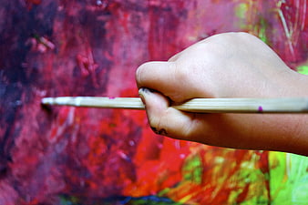 Child's hand holding paintbrush against colorful abstract painting background