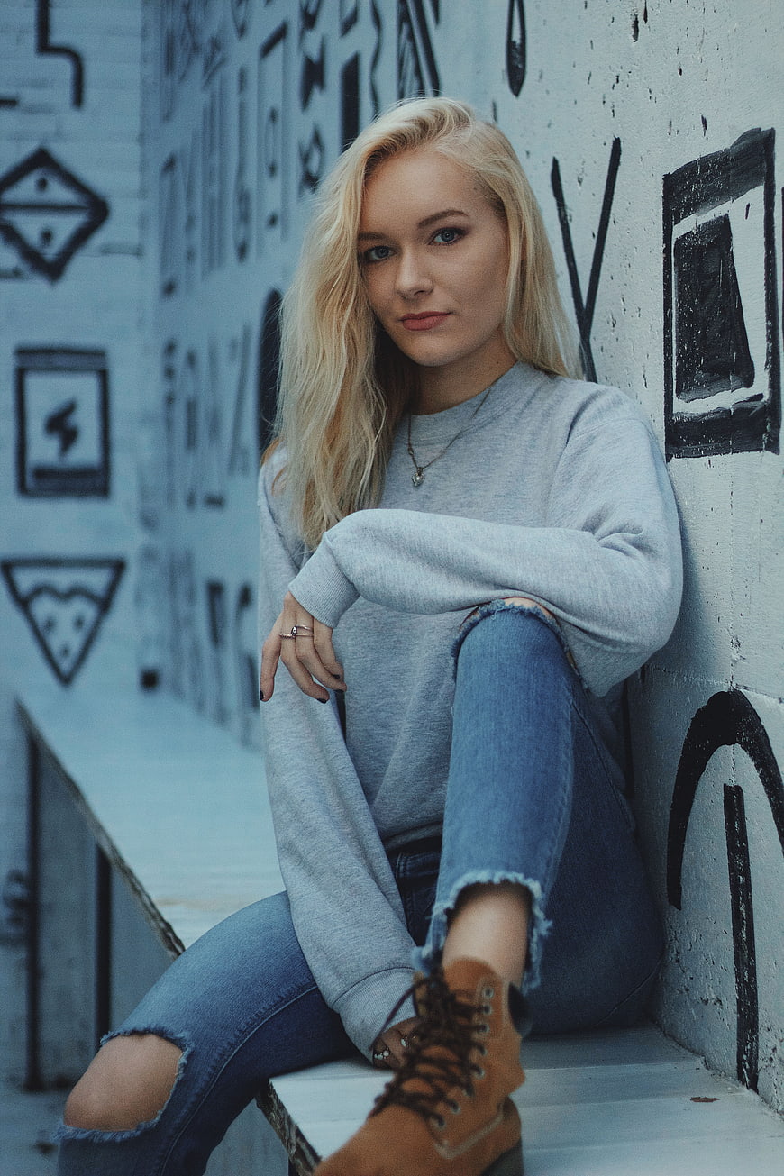 Blonde woman in ripped jeans sitting against graffiti wall
