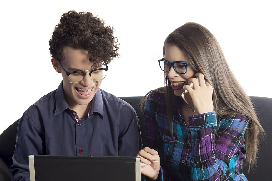 Young couple with braces smiling at laptop and phone