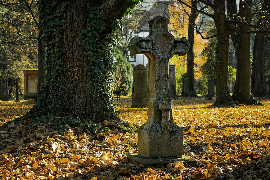 Weathered stone cross in autumn cemetery with golden leaves