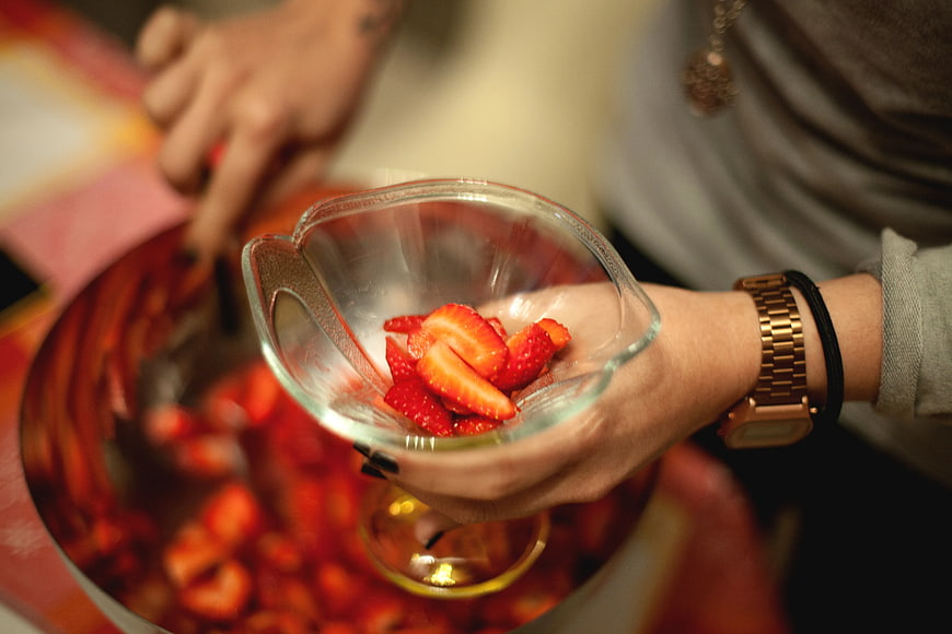 Hands holding glass bowl of sliced strawberries