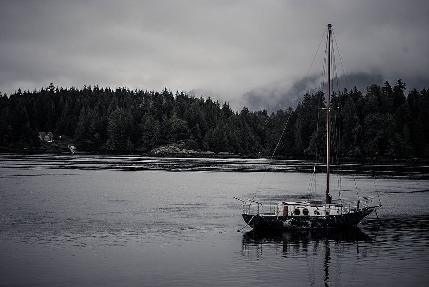 Solitary sailboat anchored in misty fjord with forested mountains