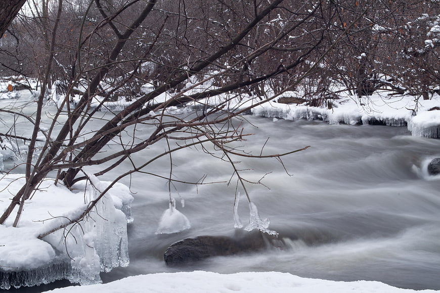 Winter river flowing through snowy forest with ice formations