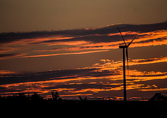Silhouette of wind turbine against dramatic orange sunset sky