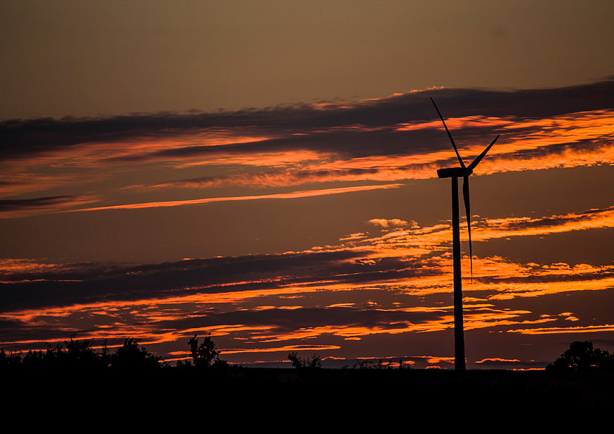 Silhouette of wind turbine against dramatic orange sunset sky