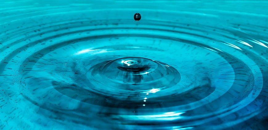 Macro shot of water droplet creating ripples in blue liquid