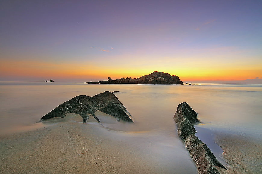 Long Exposure Sunset Beach with Silhouetted Rocks and Misty Ocean
