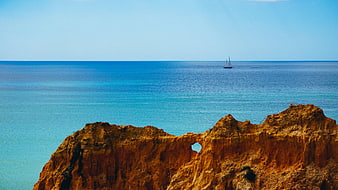 Sailboat on Blue Ocean Behind Orange Rocky Cliffs