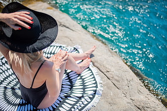 Woman in black swimsuit relaxing on rocky beach