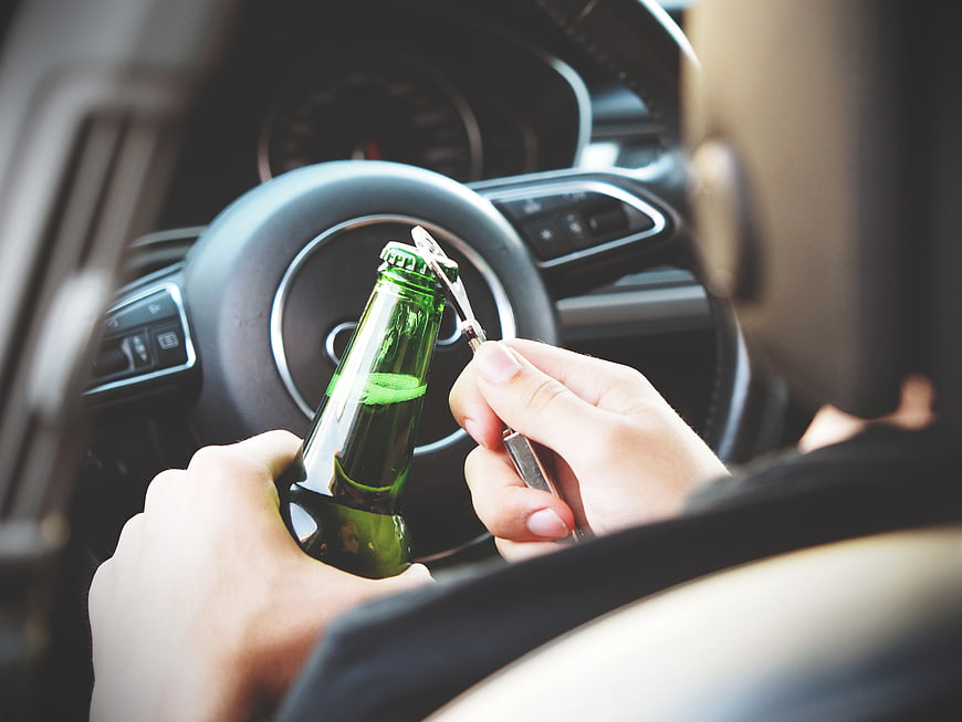 Person opening beer bottle in car driver seat