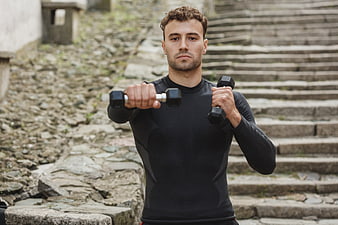 Athletic Man Lifting Dumbbells Outdoors on Stone Steps