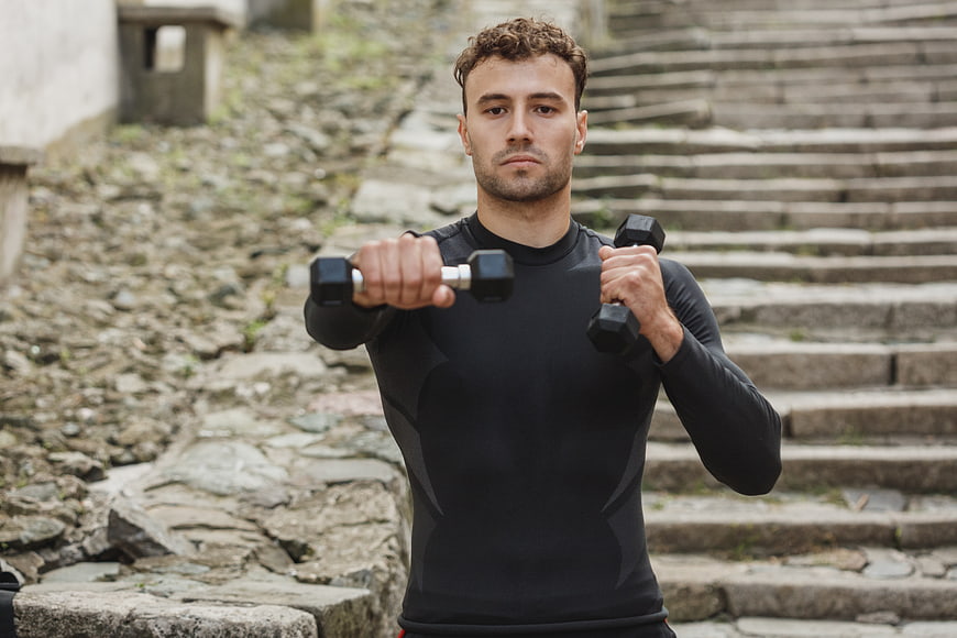 Athletic Man Lifting Dumbbells Outdoors on Stone Steps