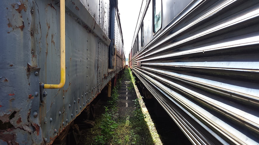 Rusty train car and modern passenger train in narrow railway corridor